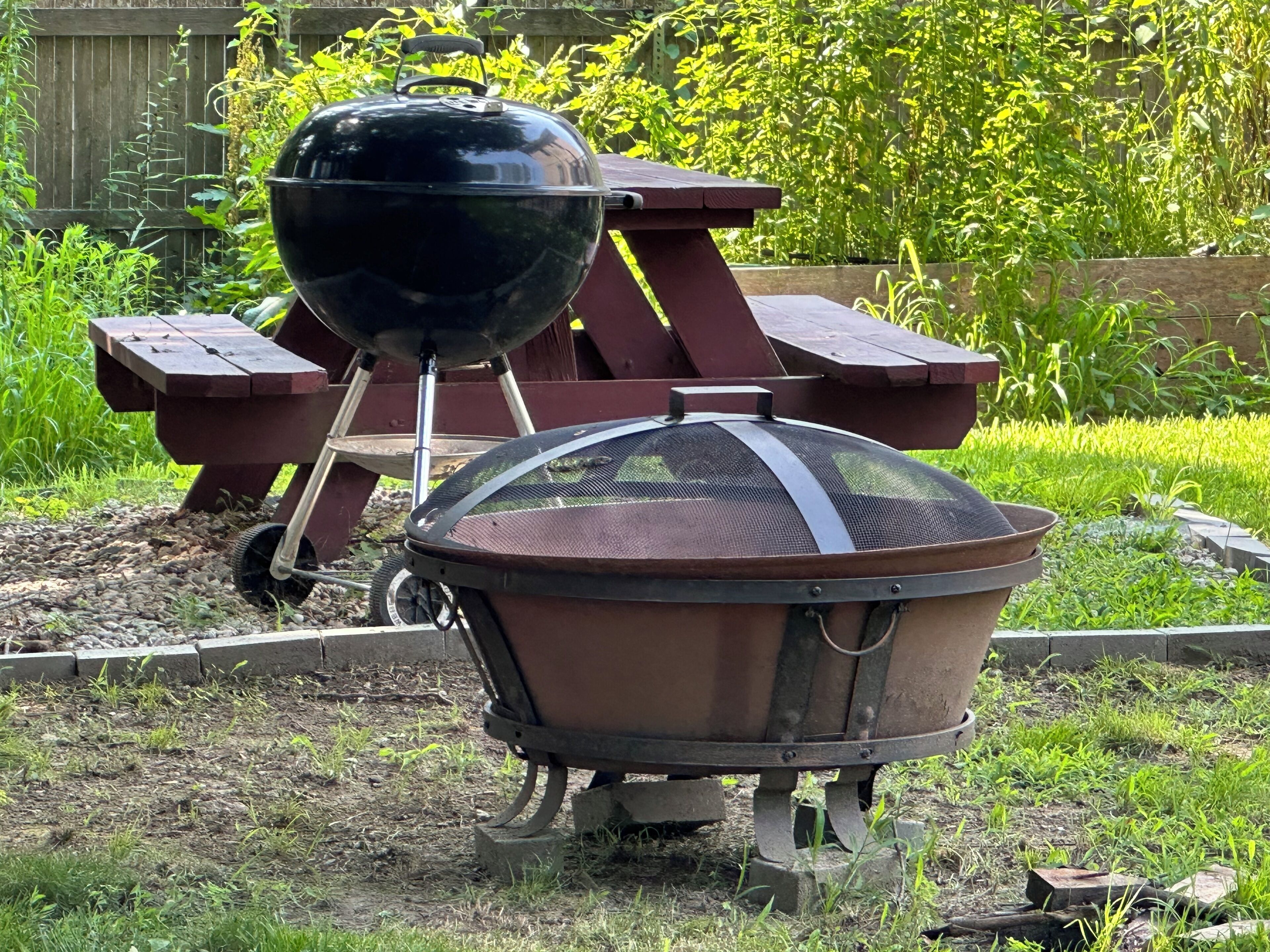 Una parrilla portátil con tapa y un carretilla en un jardín.