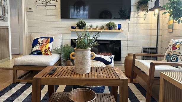 A living room with a fireplace, a television mounted on the wall, and a variety of decorative items including plants and a large vase. - Charming Retreat (Gloucester)