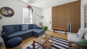 A living room with a sectional sofa, a coffee table, a wooden bench, and a wall-mounted heater. - Charming Retreat (Gloucester)