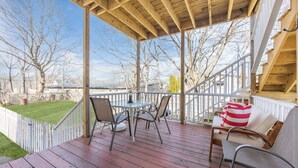 A wooden deck with a table and chairs, a white railing, and a view of trees and a distant building. - Charming Retreat (Gloucester)