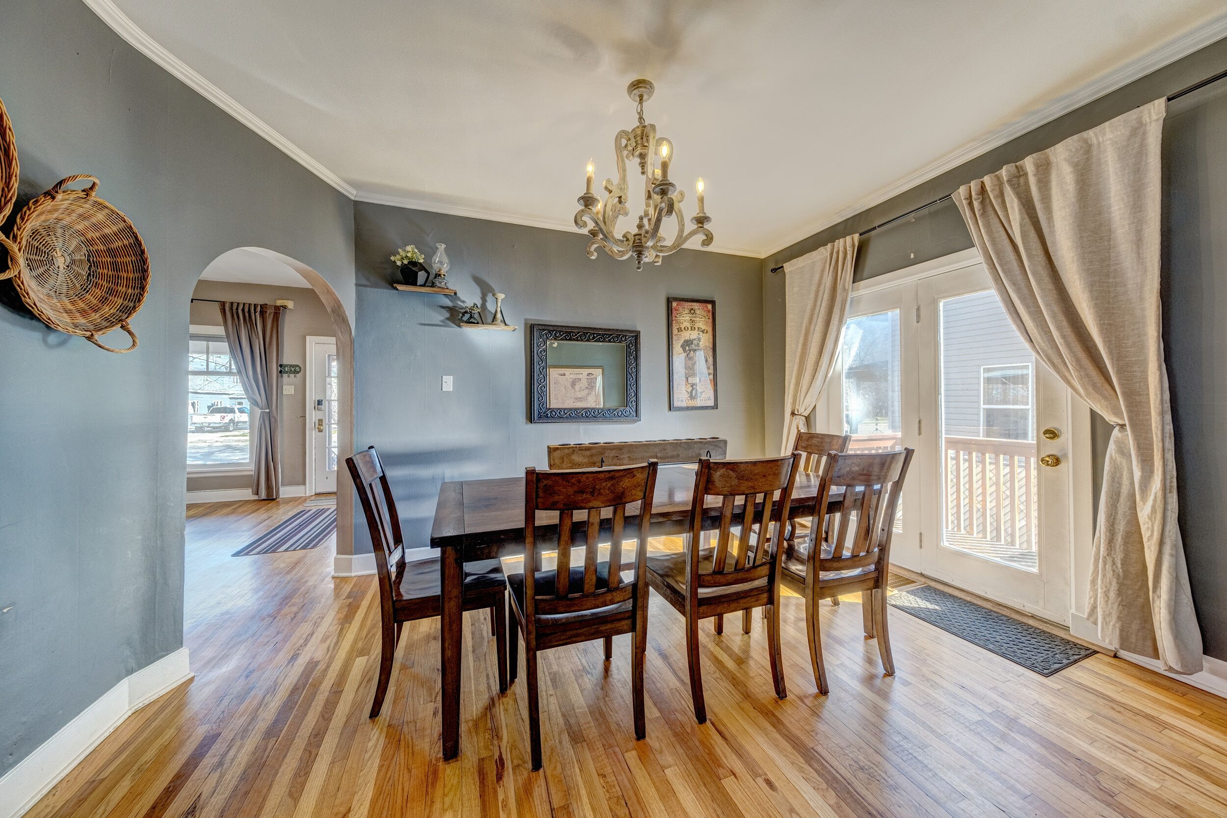 A dining room with a wooden table and chairs, a chandelier, and a view through a glass door.