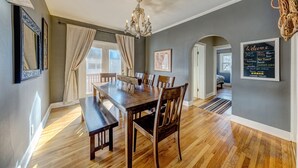 Un coin repas avec une table et des chaises en bois, un lustre et un panneau d’accueil accroché au mur.