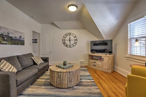 Un salon avec un canapé, une table basse, un téléviseur et une horloge au mur.
