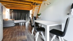 Un comedor con una mesa blanca, sillas negras, techo de madera y una escalera.