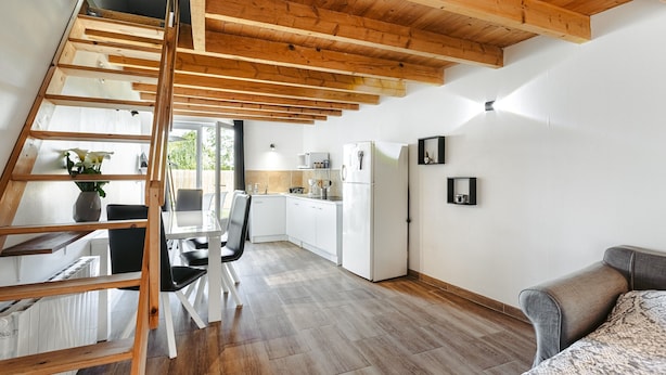 Una cocina moderna con armarios blancos, techo de madera y zona de comedor con mesa y sillas.