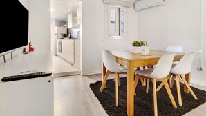 A modern kitchen with white cabinets, a dining area with a wooden table and white chairs, and a TV on a stand. - Prestigegoldresidence 1 – Historic Center Apartment with Wi-Fi and Air Conditioning (Guimarães)
