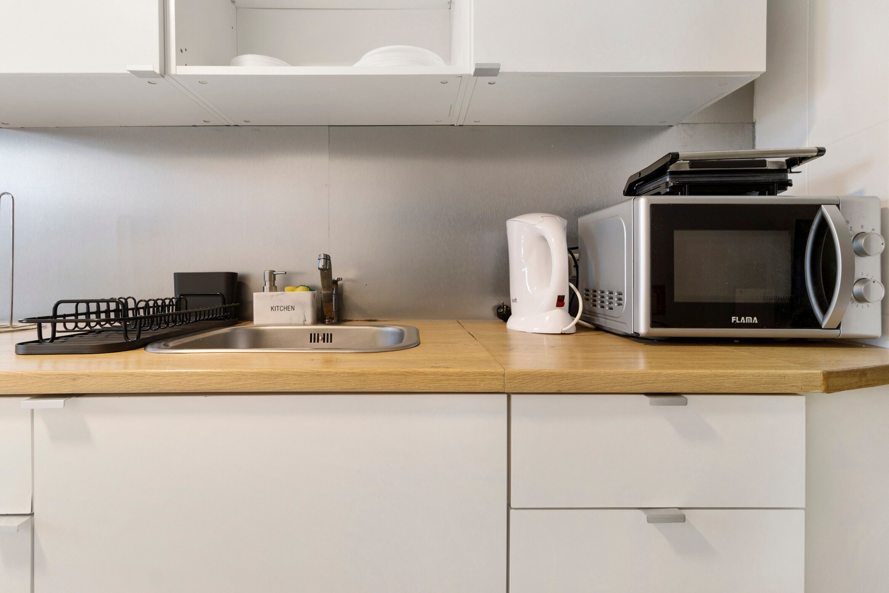 Cozinha equipada com micro-ondas, chaleira e máquina de café no balcão.