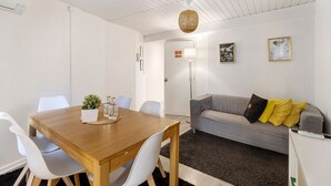 A room with a wooden dining table, white chairs, a grey sofa with yellow pillows, a floor lamp, and framed pictures on the wall. - Prestigegoldresidence 1 – Historic Center Apartment with Wi-Fi and Air Conditioning (Guimarães)