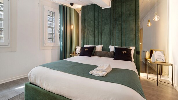A neatly made bed with a green and white bedspread, a bedside table with a lamp, and a framed certificate on the wall. - Prestigegoldresidence 1 – Historic Center Apartment with Wi-Fi and Air Conditioning (Guimarães)
