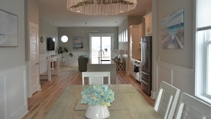 A modern kitchen with a dining area, featuring a central island, white cabinetry, and a hanging light fixture.