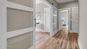 A hallway with wooden flooring, white doors, and a blue-striped bag on the floor.