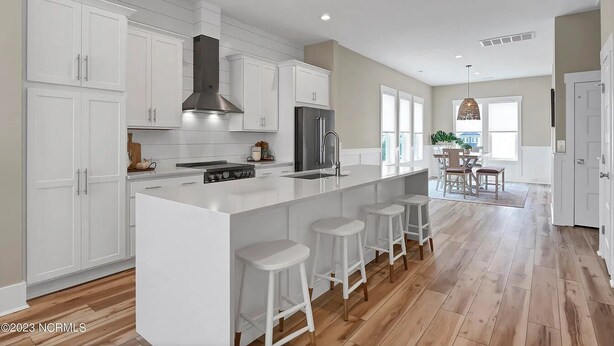 A modern kitchen with white cabinetry, a central island with stools, a large stove, and a refrigerator.