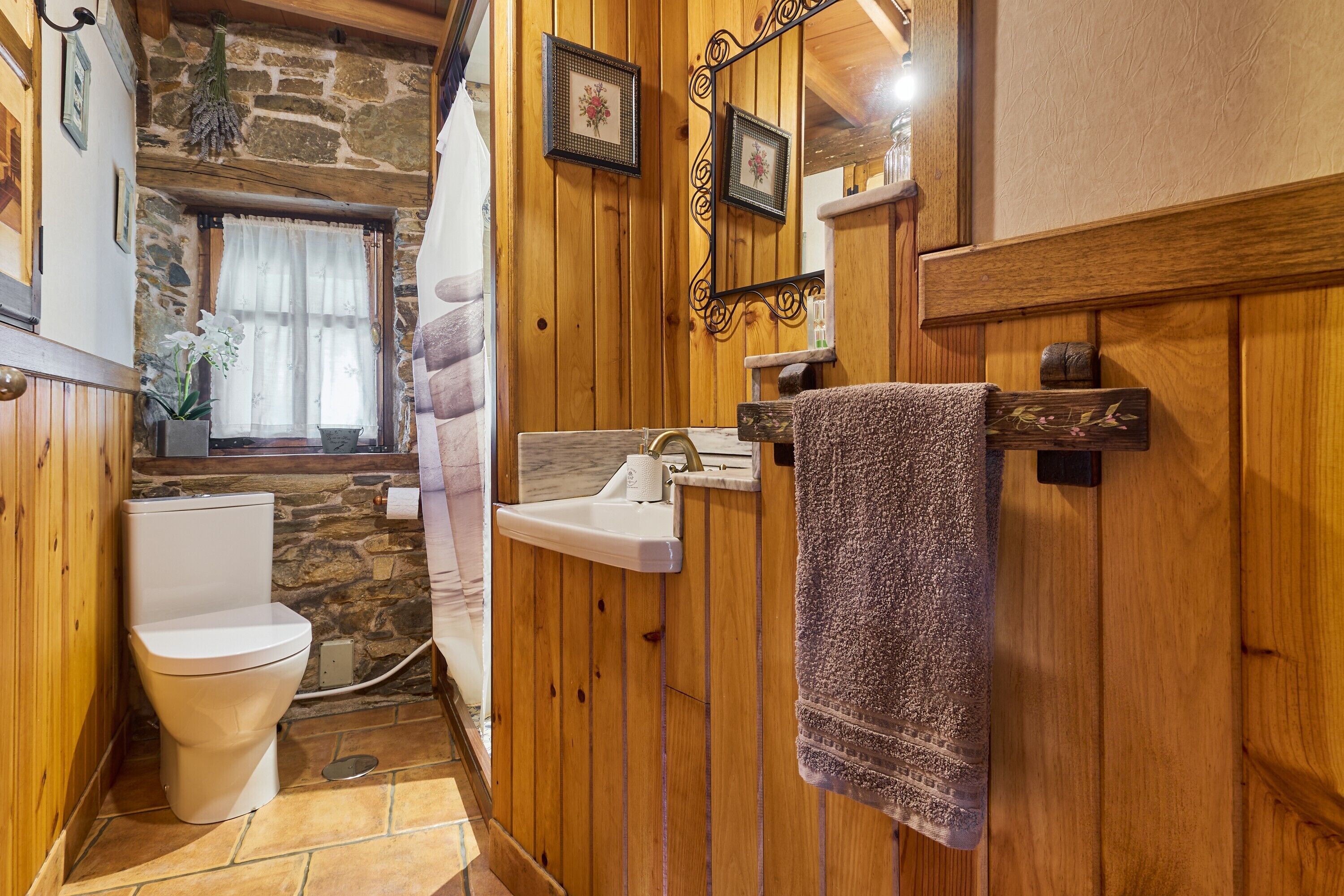 A bathroom with a stone wall, wooden paneling, a white toilet, a sink, and a towel rack.