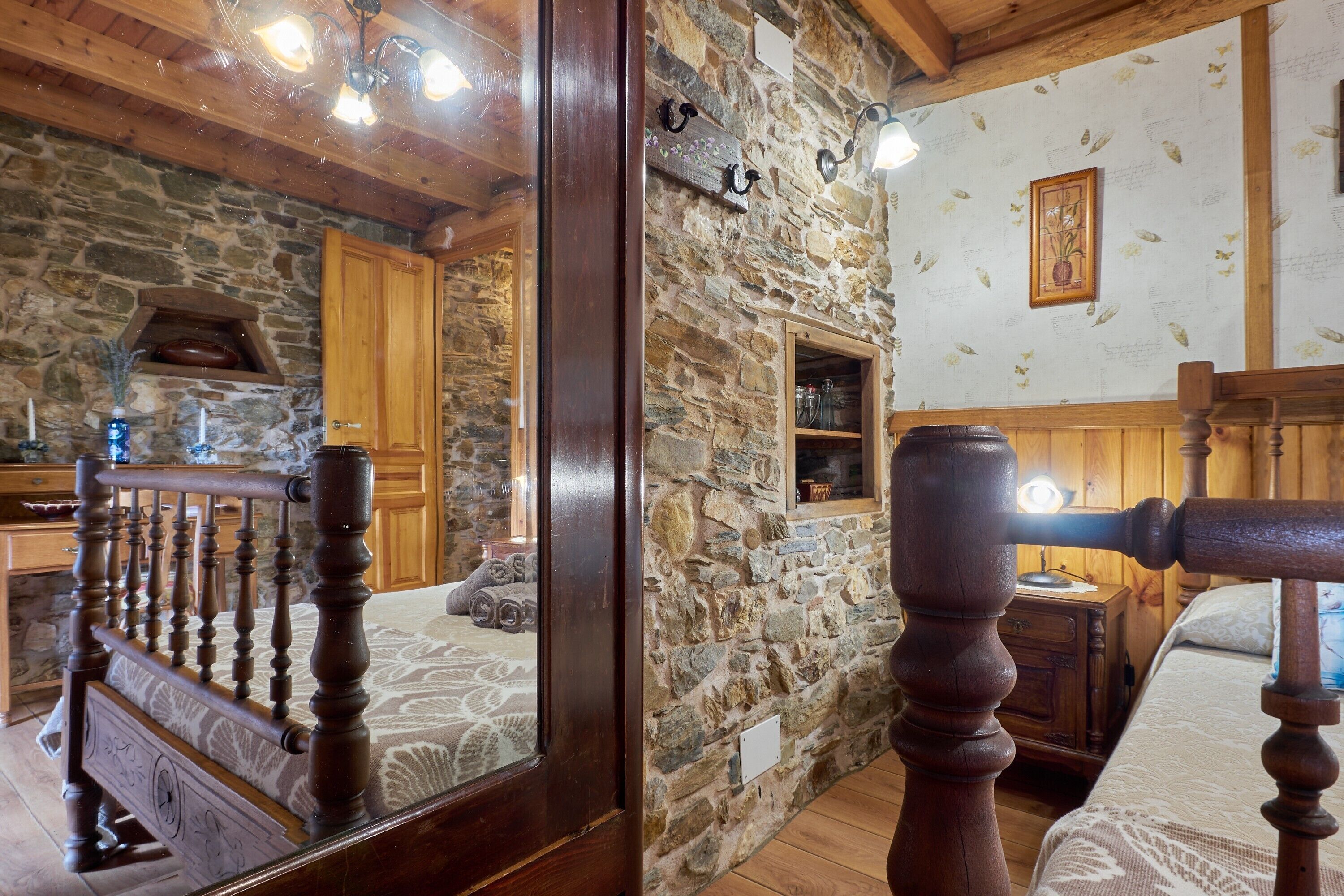 Una habitación rústica con paredes de piedra, vigas de madera, una cama con cabecera de madera y una silla de madera.