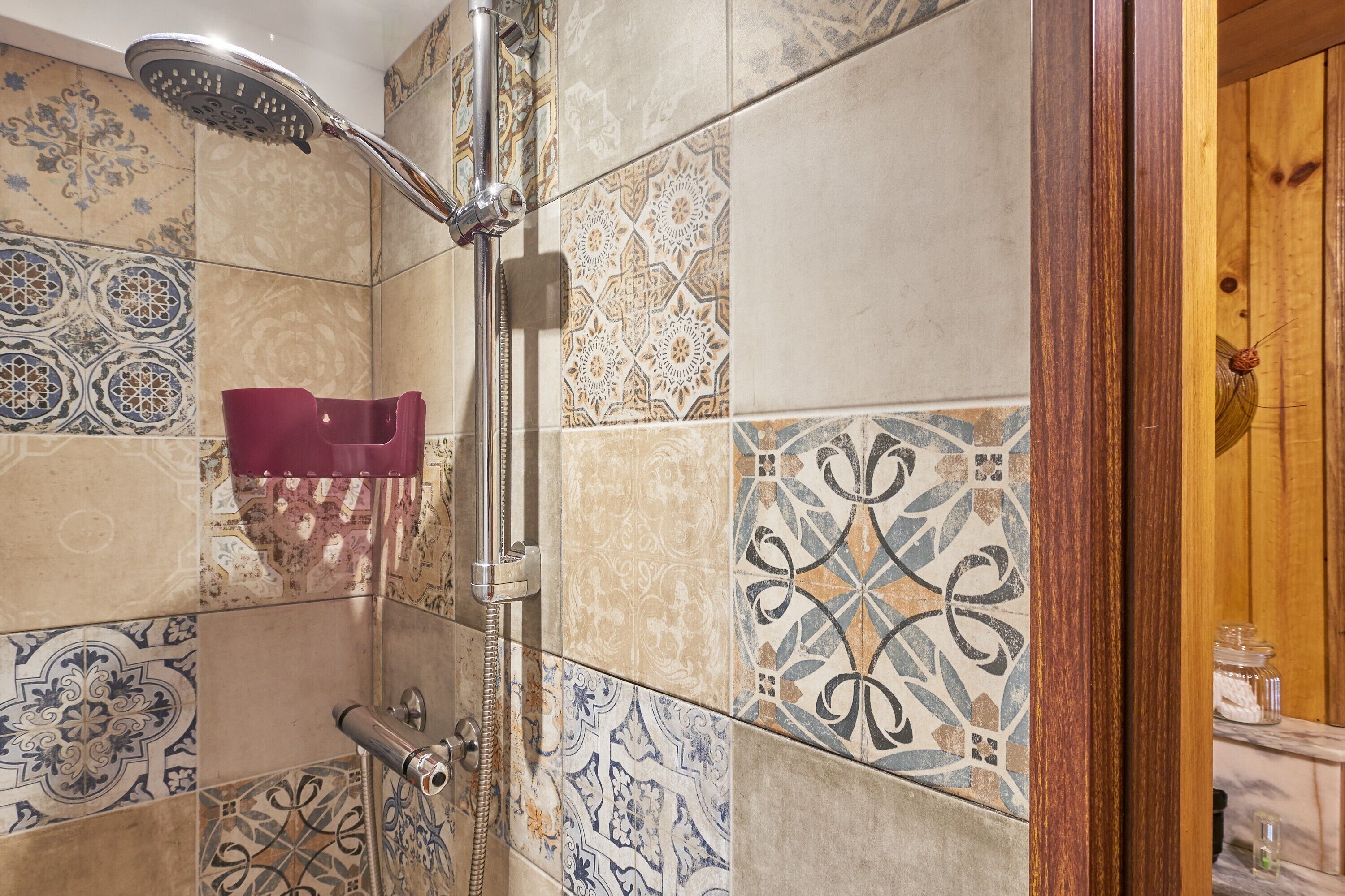 A bathroom with a shower, a red towel rack, and patterned tiles.