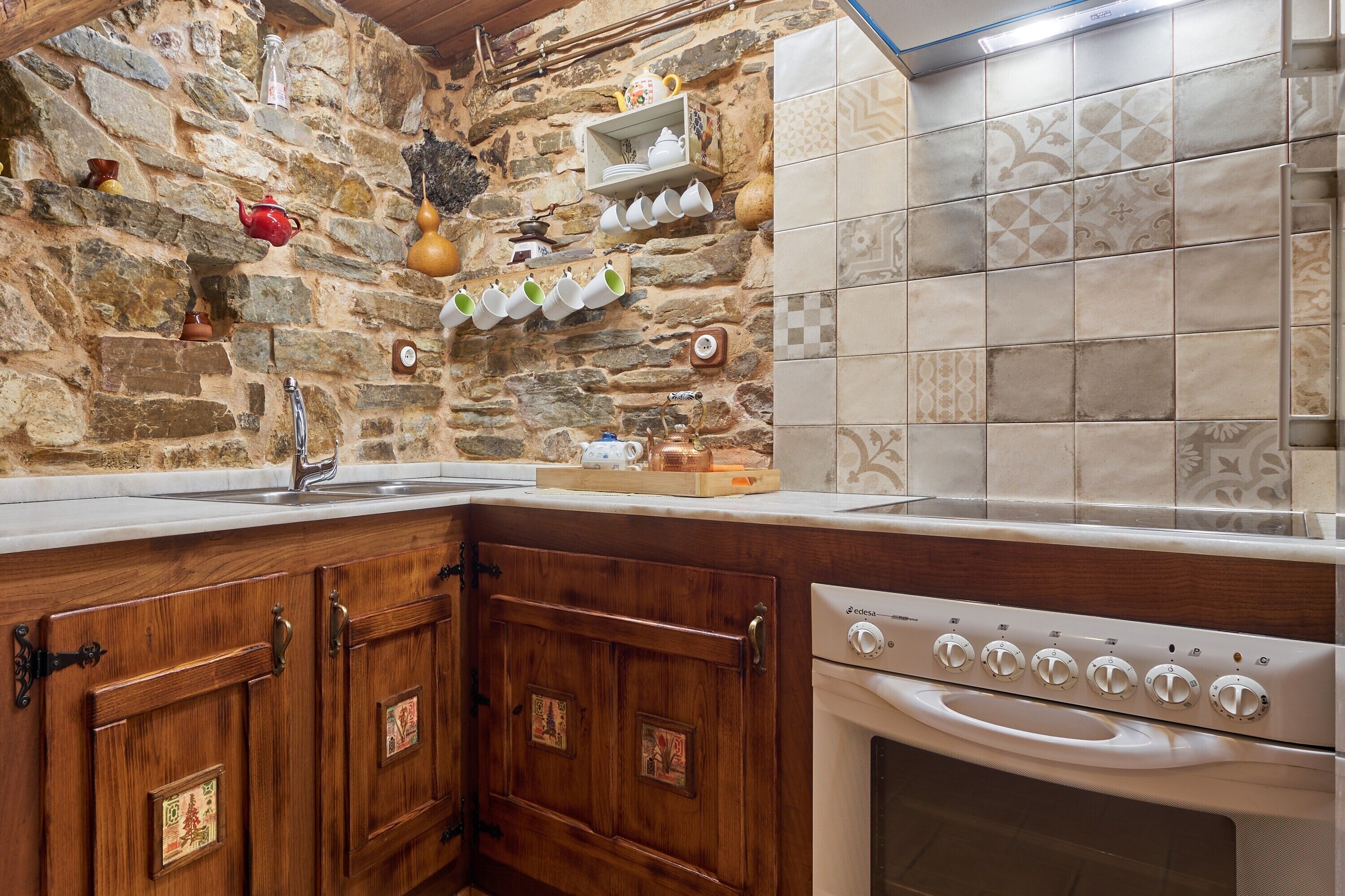 Una cocina con pared de piedra, armarios de madera, horno empotrado y salpicadero de azulejos.