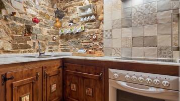 Una cocina con pared de piedra, armarios de madera, horno empotrado y salpicadero de azulejos.