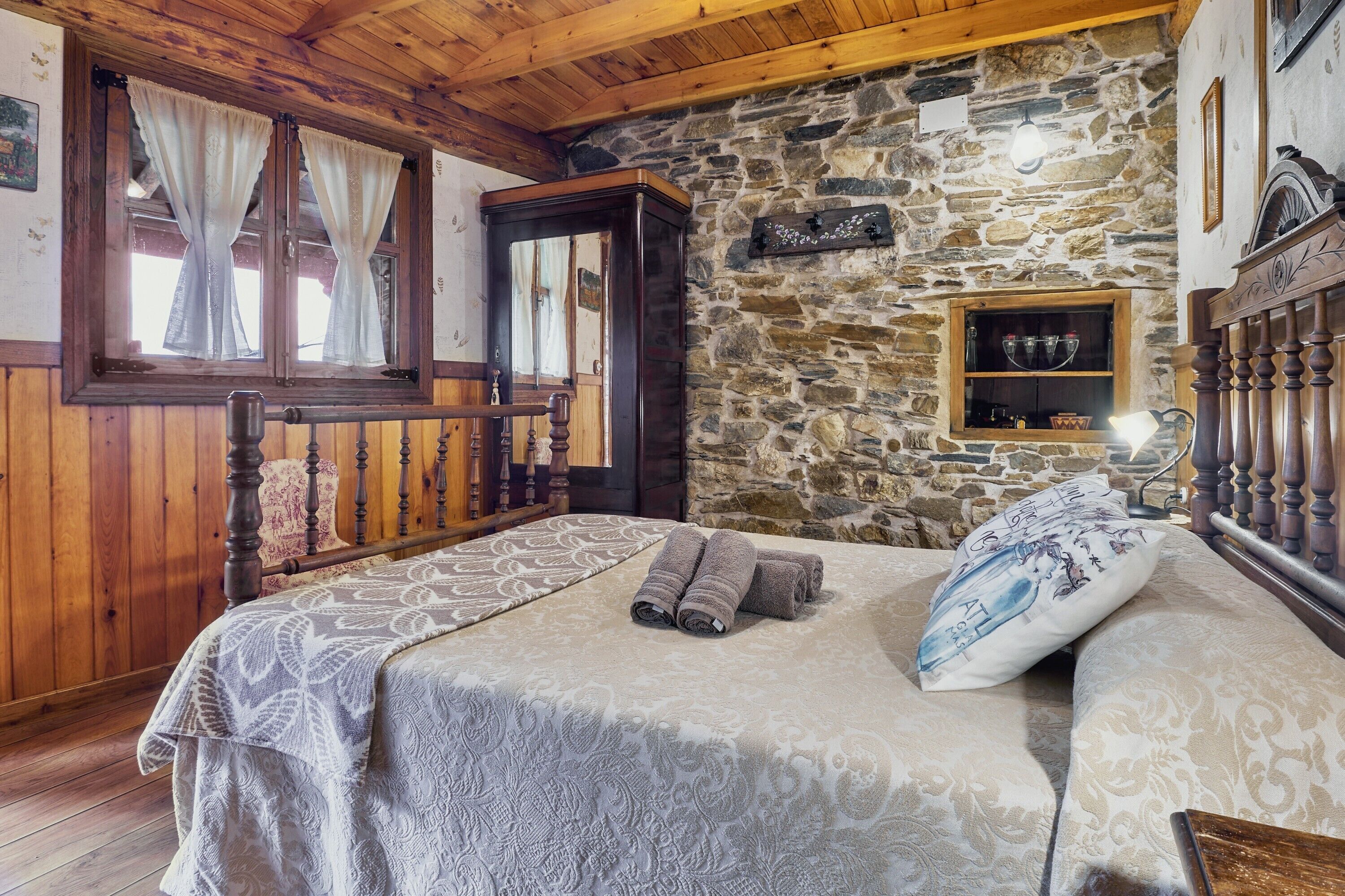 Ein Zimmer mit einem Bett, einem Holzkopfteil, einer Steinwand und einem kleinen Regal mit Gegenständen.