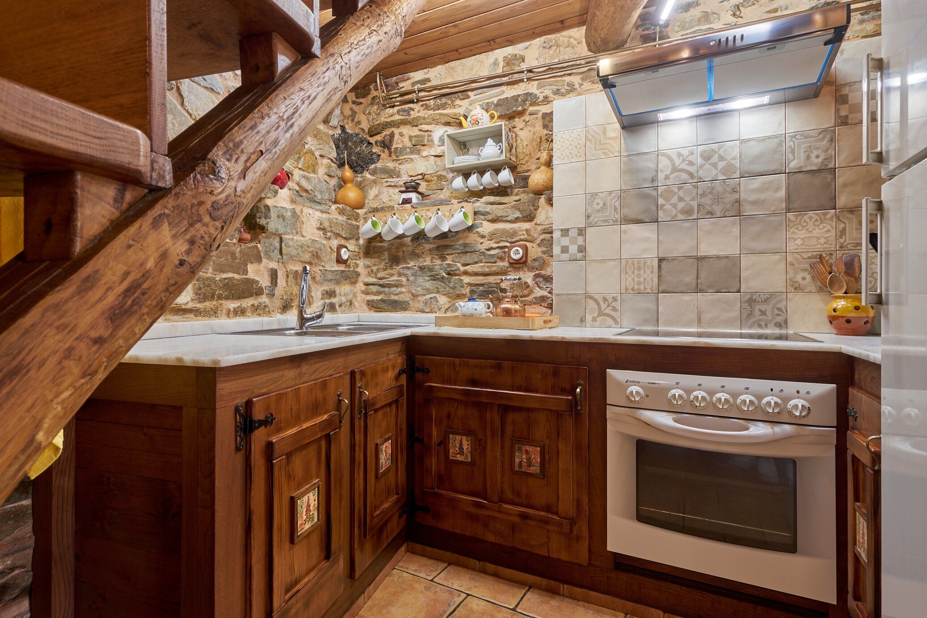 A kitchen with wooden cabinets, a stone wall, and a tiled backsplash.