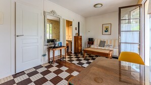 A room with a checkered floor, a wooden dining table, a yellow chair, a sofa, a mirror, and a door. - Charming Studio Cap Ferret Phare (Lège-Cap-Ferret)