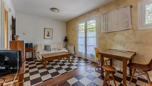 A living room with a checkered floor, a sofa, a coffee table, a TV, and a dining area with a table and chairs. - Charming Studio Cap Ferret Phare (Lège-Cap-Ferret)