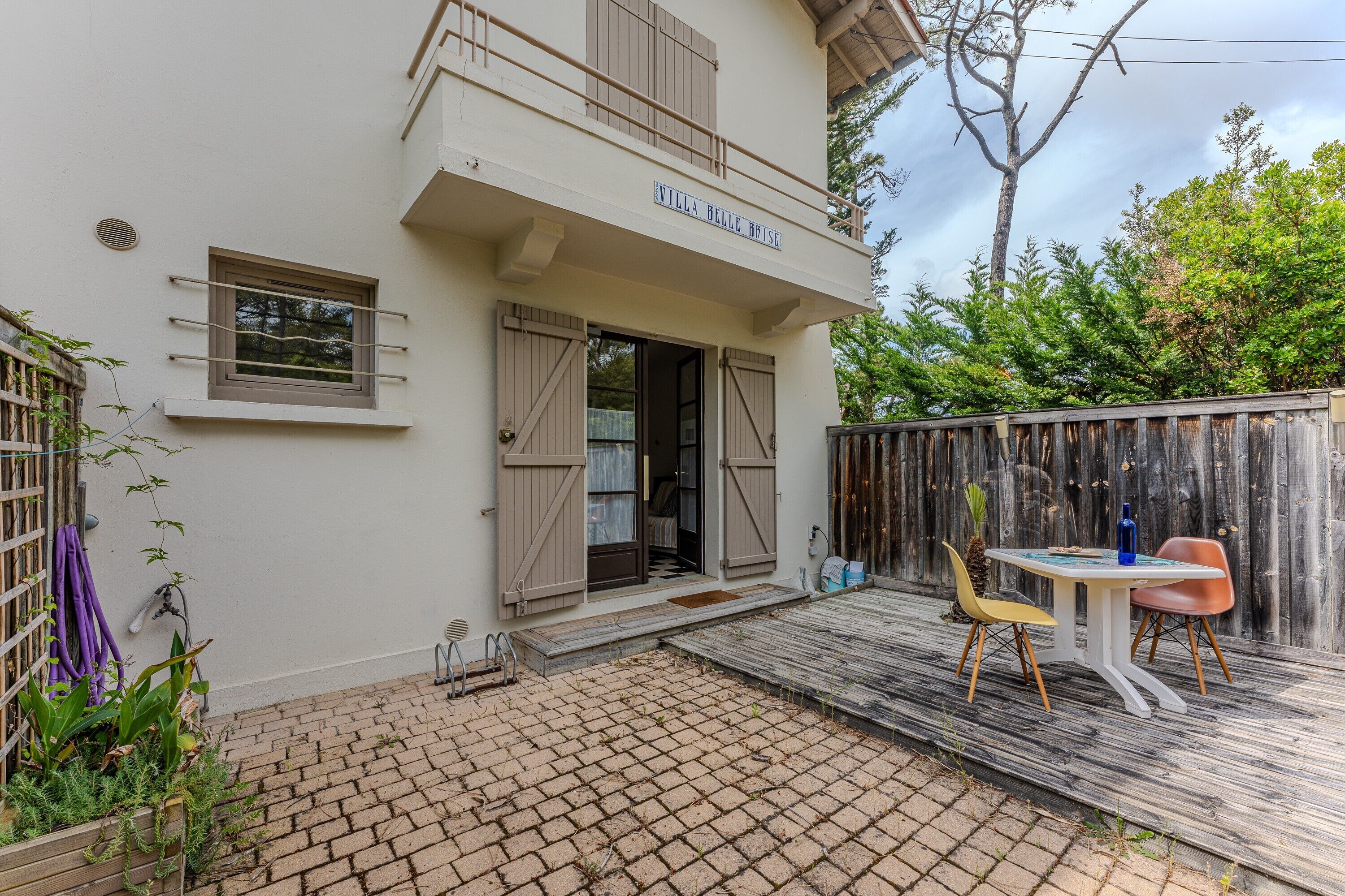 A villa named 'Villa Belle Brise' with a paved patio, outdoor seating, and a wooden fence.