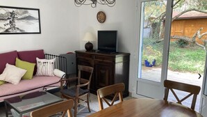Una sala de estar con sofá, sillas, una mesa, televisor y vistas al exterior.