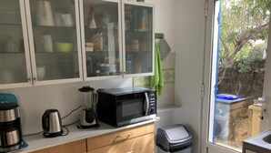 Una cocina compacta con microondas, hervidor de agua y licuadora en la encimera, un cubo de basura y una puerta que da a un área exterior.