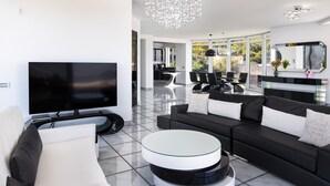 A modern living room with a flat-screen TV, a glass coffee table, a black sofa, and a chandelier. - Apartment "Villa Coral - First Floor" with Private Pool & Wi-Fi (Chamolia)