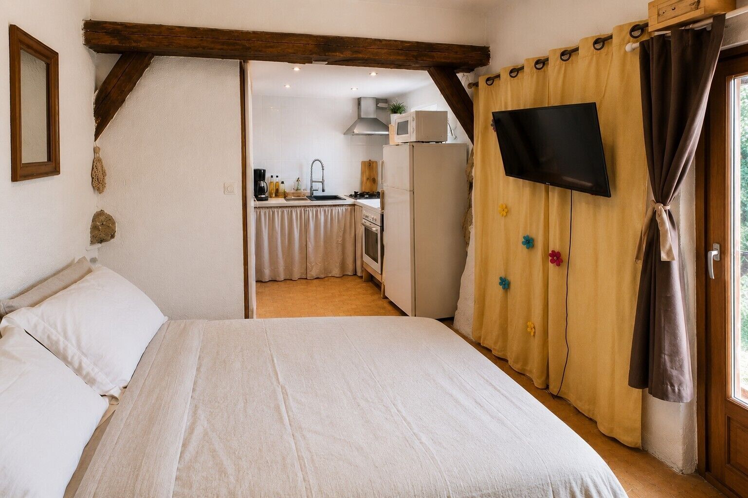 Ein Schlafzimmer mit Bett, einem an der Wand befestigten Fernseher und einer Küche im Hintergrund.