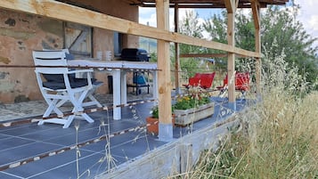 Un área de estar al aire libre con estilo rústico, que incluye una mesa, sillas, una parrilla y vistas del paisaje circundante.