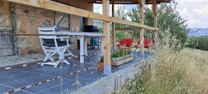 Un espace extérieur aménagé dans un style rustique, avec une table et des chaises, un barbecue et une vue sur le paysage environnant.