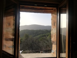 Quarto com uma grande janela que mostra um morro arborizado.