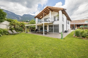 A two-story house with a covered patio, a lawn, and mountains in the background.