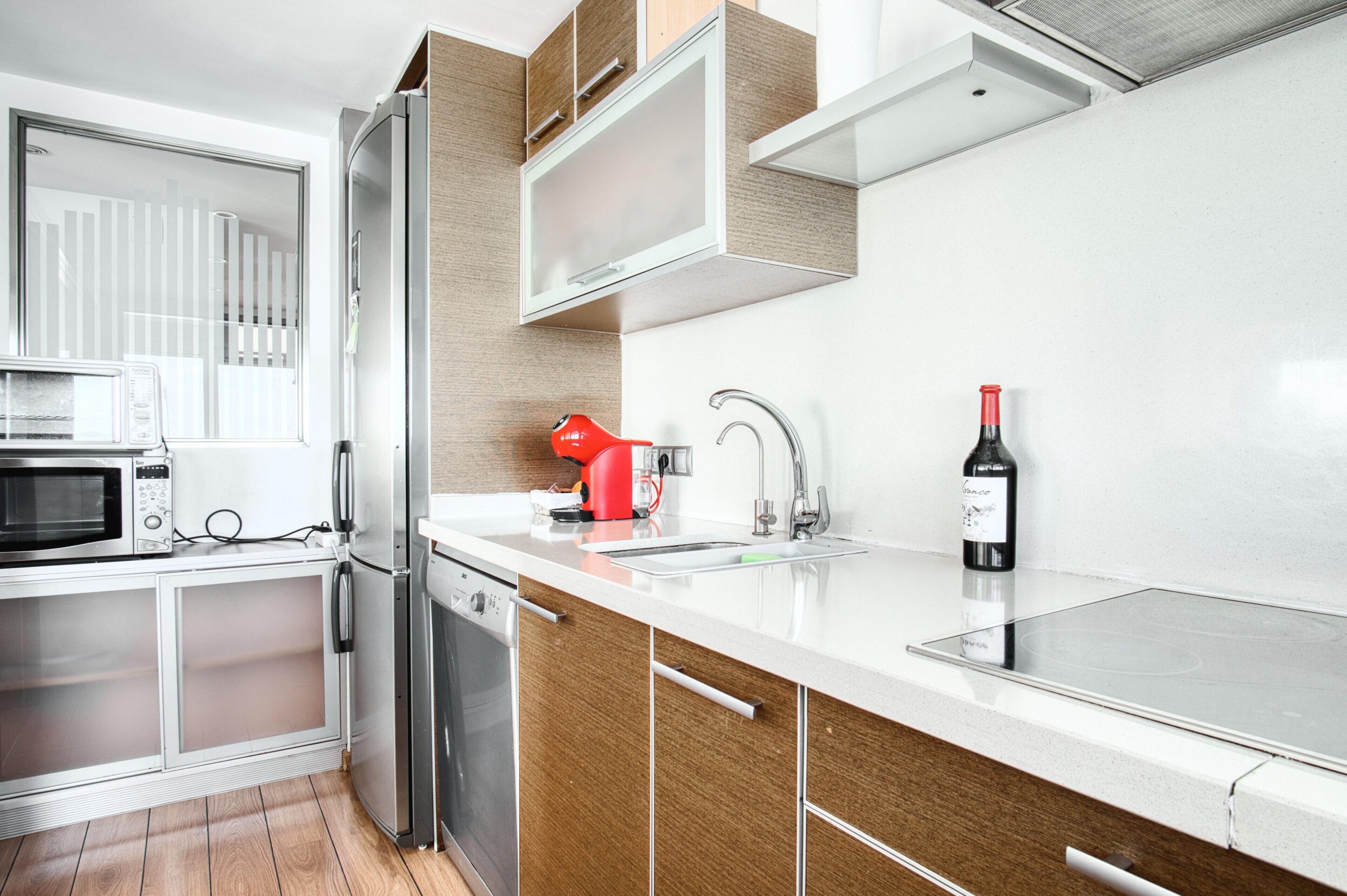 Una cocina moderna con microondas, refrigerador, hervidor rojo, botella de vino y lavavajillas.