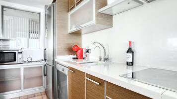 Una cocina moderna con microondas, refrigerador, hervidor rojo, botella de vino y lavavajillas.