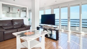 A modern living room with a leather sofa, a glass coffee table, a flat-screen TV, and large windows offering a view of the sea. - Apartment 'Andres' with Sea View, Wi-Fi and Air Conditioning (El Campello)