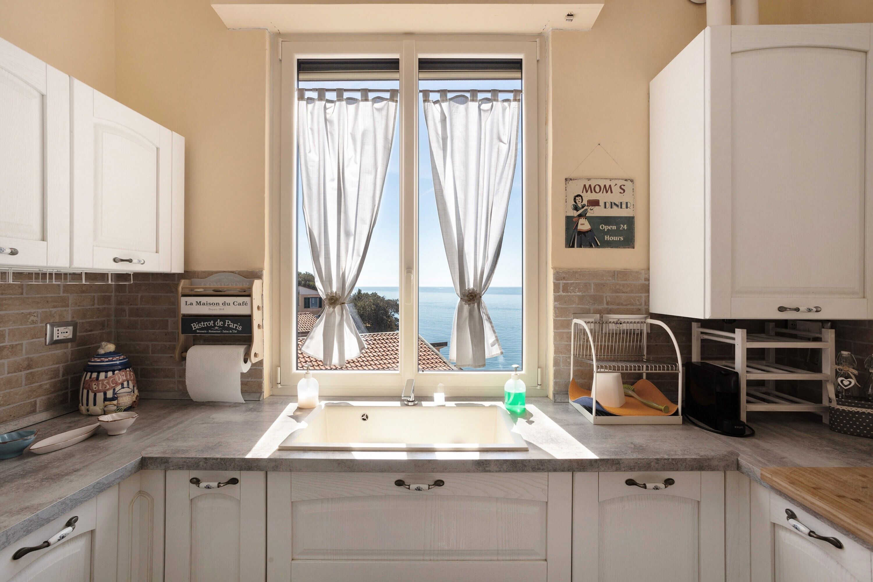A kitchen with a large window, white cabinets, and a view of the sea.