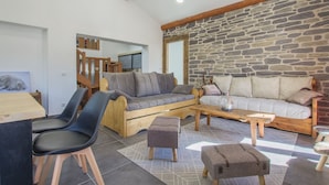 A cozy living area with a stone wall, wooden furniture, and a view of a staircase. - Gîte Les Mélèzes – Mountain Views, Balcony & Wi-Fi (TERMIGNON)