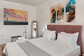 Habitación de hotel con una cama grande, un espejo montado en la pared y dos cuadros abstractos.