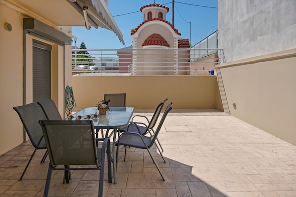 Un patio con una mesa y sillas, una puerta cerrada y vista a un edificio con fachada roja y blanca.