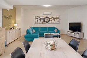 Una sala de estar con un sofá color turquesa, una mesa de comedor con sillas, un televisor sobre un mueble bajo y una obra de arte con un mapa mundial en la pared.