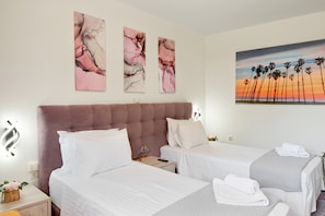 A hotel room with two beds, a large headboard, artwork on the wall, and a painting of palm trees. - Apartment "Theo and Ms Luxurious" with Private Terrace & Wi-Fi (Kos)