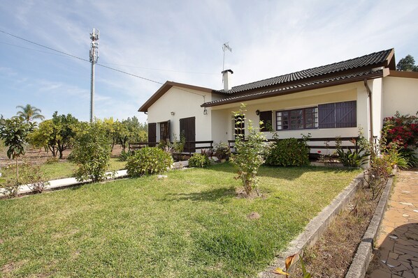 A single-story house with a tiled roof, a front porch, and a small garden with various plants and a lawn.