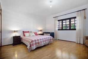 A bedroom with a bed, bedside tables, a window with curtains, and a wooden floor.