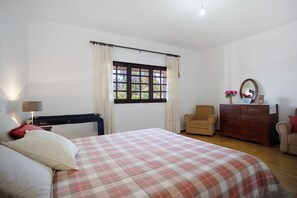 A bedroom with a bed, a dresser, a chair, a window with curtains, and a lamp.