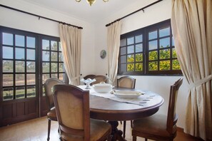 A dining area with a round table, four chairs, and two windows with curtains.