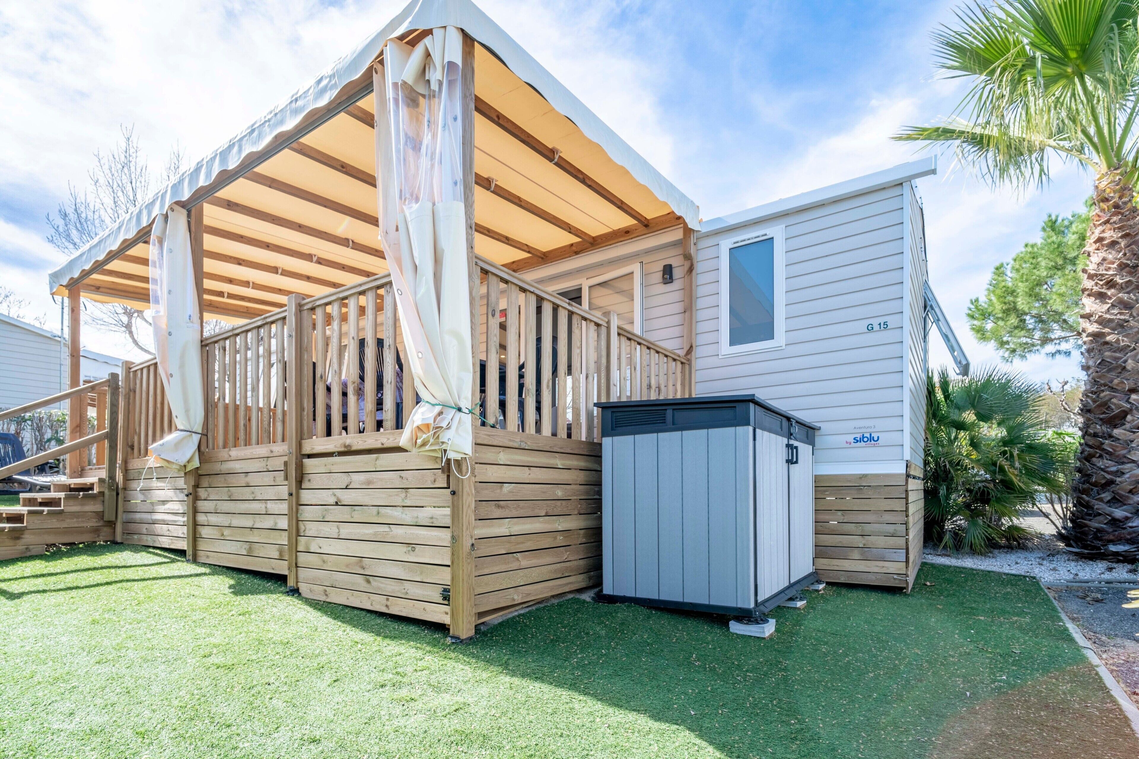 Una casa mobile con una veranda in legno, un portico coperto e un piccolo deposito annesso.
