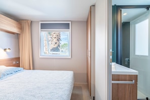 Une chambre à coucher avec un lit, une fenêtre donnant sur un beau paysage, une salle de bain avec un lavabo et une armoire.