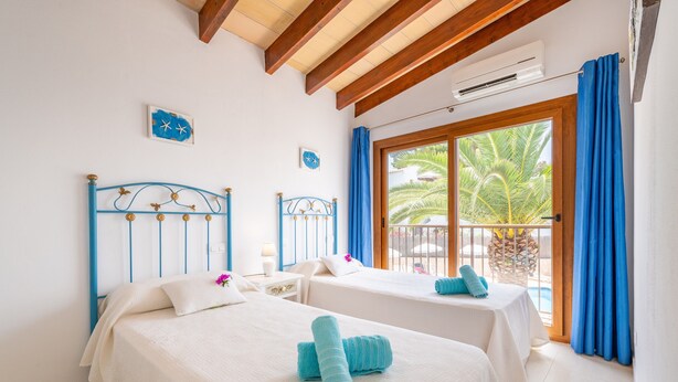 Habitación de hotel con dos camas, ventana con vista a palmeras, techo de madera y un equipo de aire acondicionado.